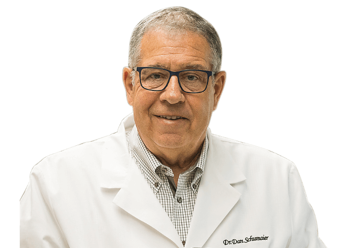 Dr. Daniel Schumaier, founder of EarTech, wearing a white lab coat and glasses, smiling at the camera.